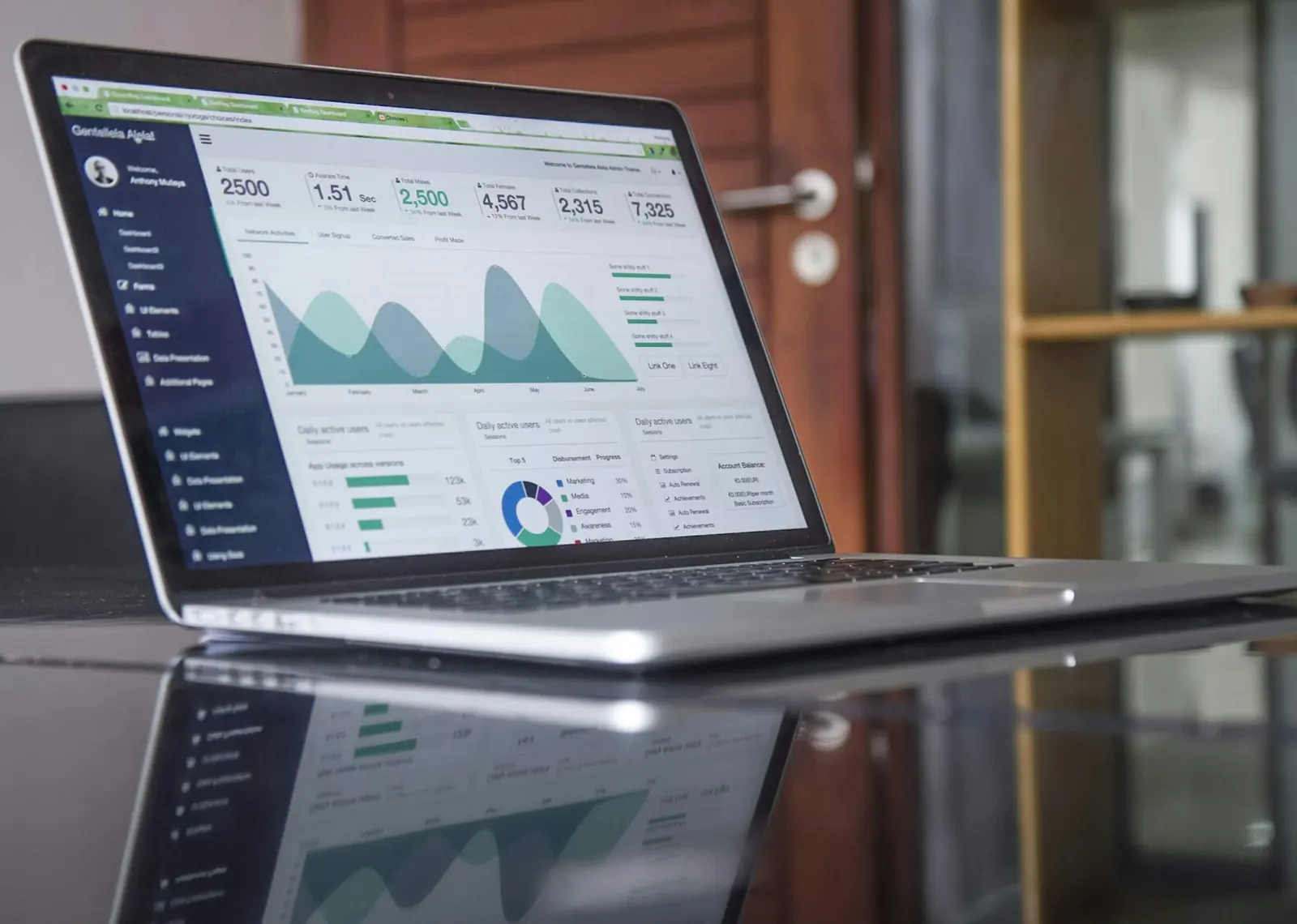 Laptop con un tablero de gráficas y pronósticos, reflejada en una mesa de vidrio